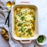 Green Chili Chicken Enchiladas in a light pink casserole dish with cilantro on the side.