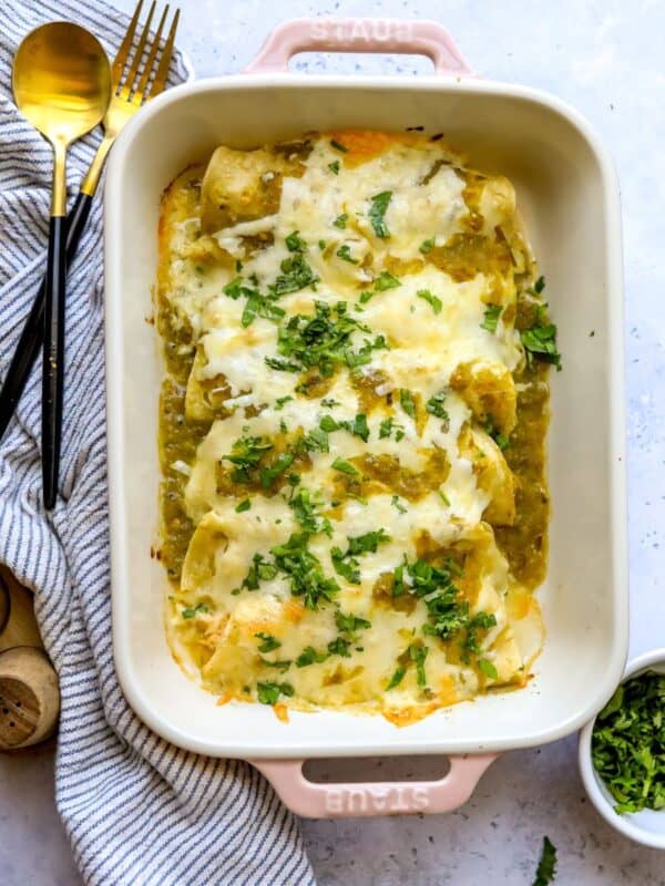Green Chili Chicken Enchiladas in a light pink casserole dish with cilantro on the side.