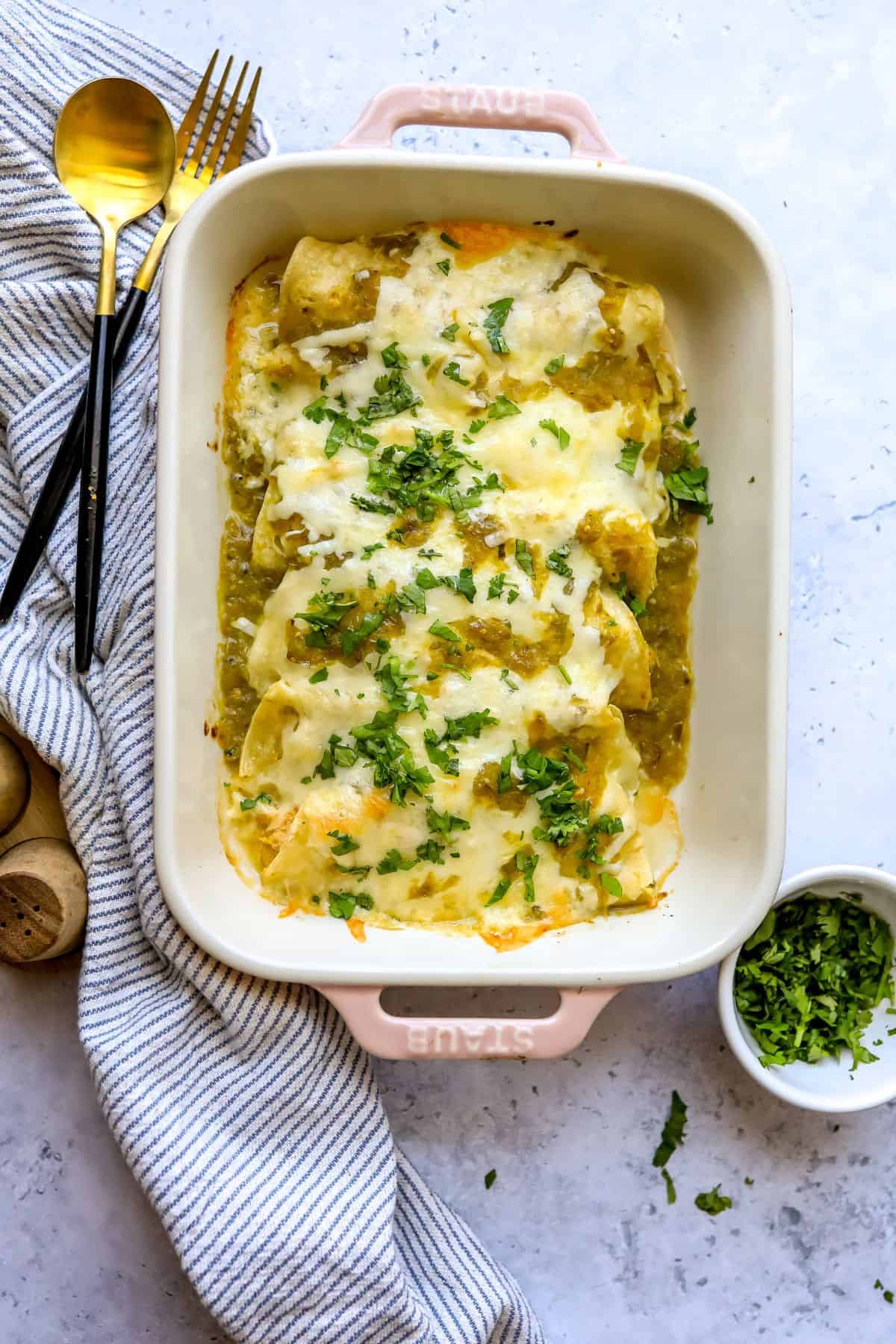 Green Chili Chicken Enchiladas in a light pink casserole dish with cilantro on the side.