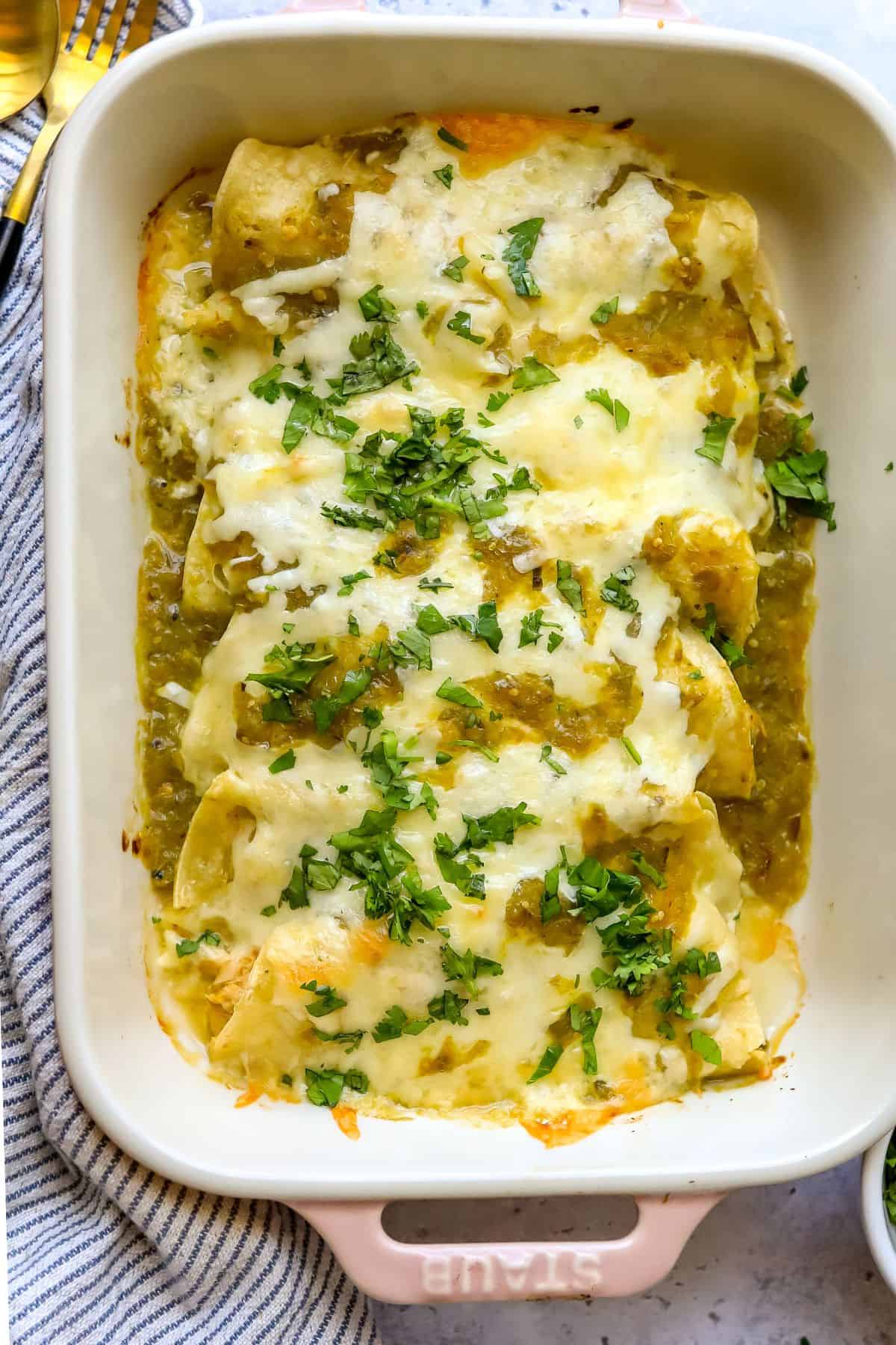 Green Chili Chicken Enchiladas in a light pink casserole dish up close.
