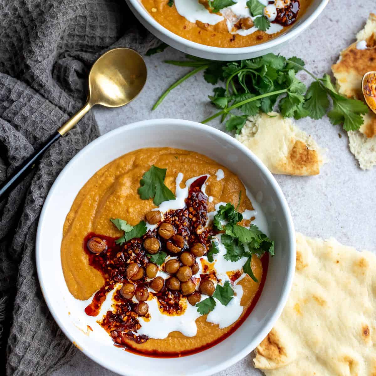 White bowls with soup in them, topped with sour cream and chickpeas. 