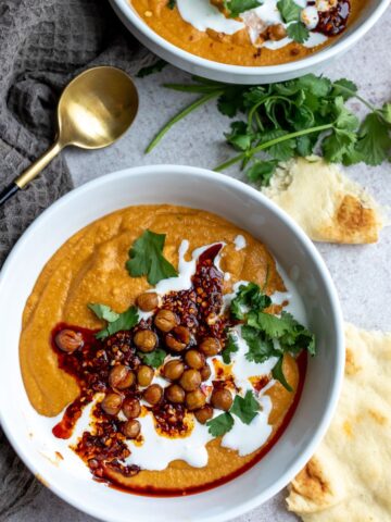 Soup in a white bowl with toppings and a gold spoon.