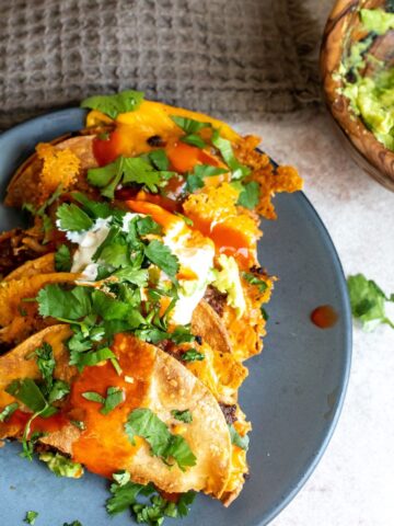 crispy tacos on a grey plate with guacamole.