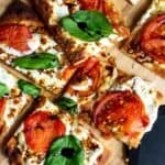 Pizza up close on a cutting board with basil.