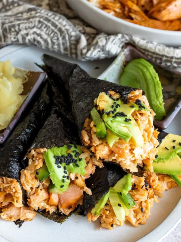 Hand rolls on a white plate with avocado.