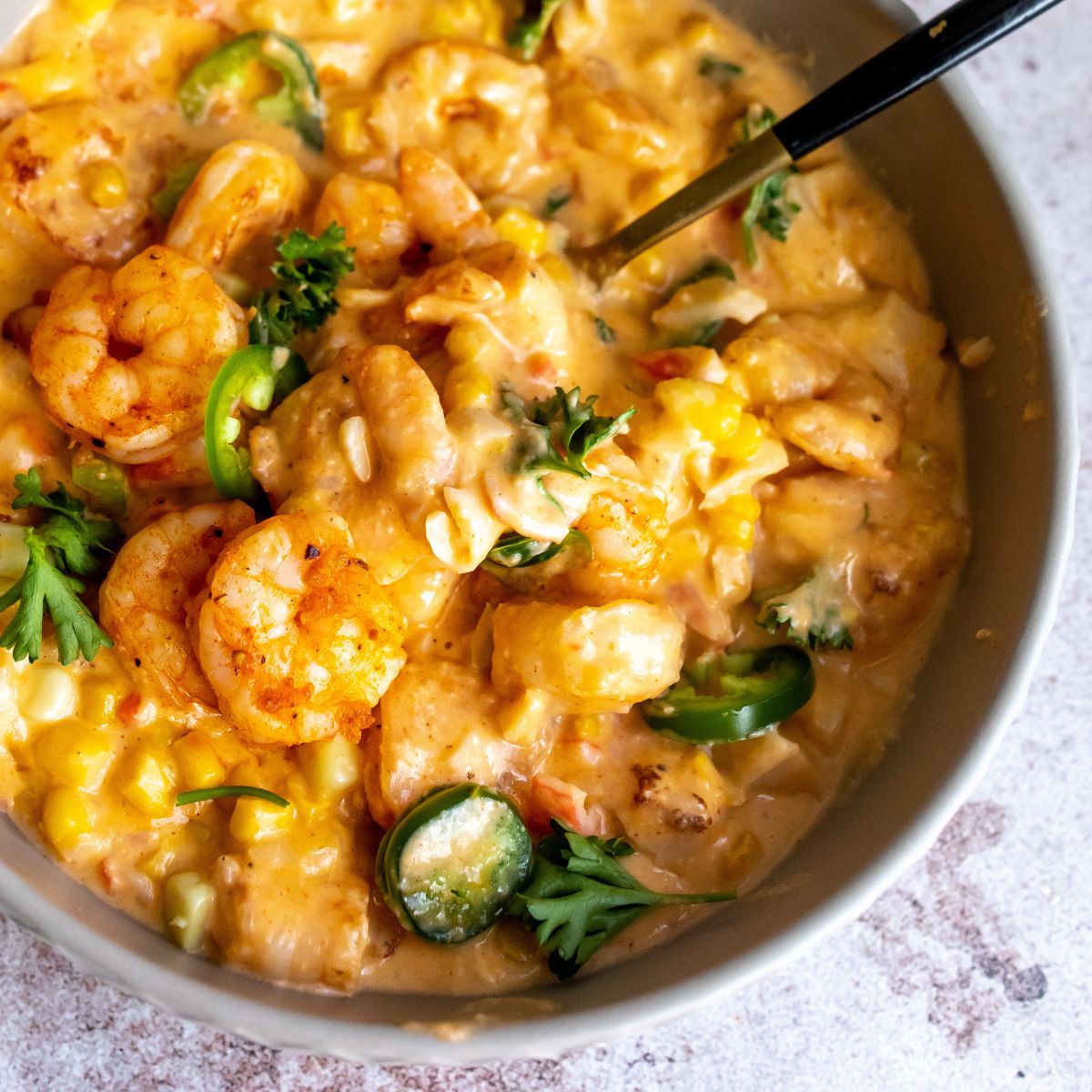 Shrimp and corn bisque up close in a bowl with a black spoon. 