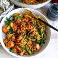 Teriyaki Salmon noodles in a white bowl with a black fork in the bowl.