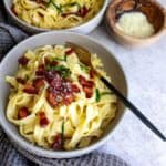 Pasta in a grey bowl with bacon and a fork.