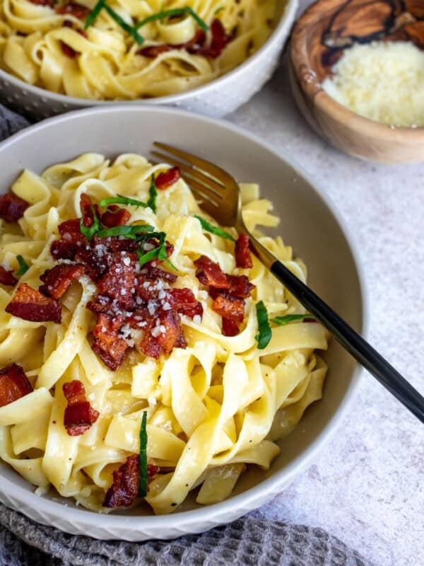 Pasta in a grey bowl with bacon and a fork.