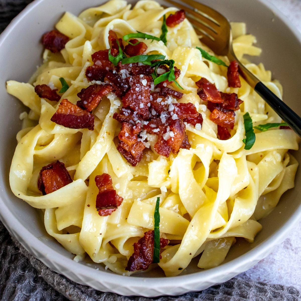 Pasta in grey bowl up close with pancetta and basil. 