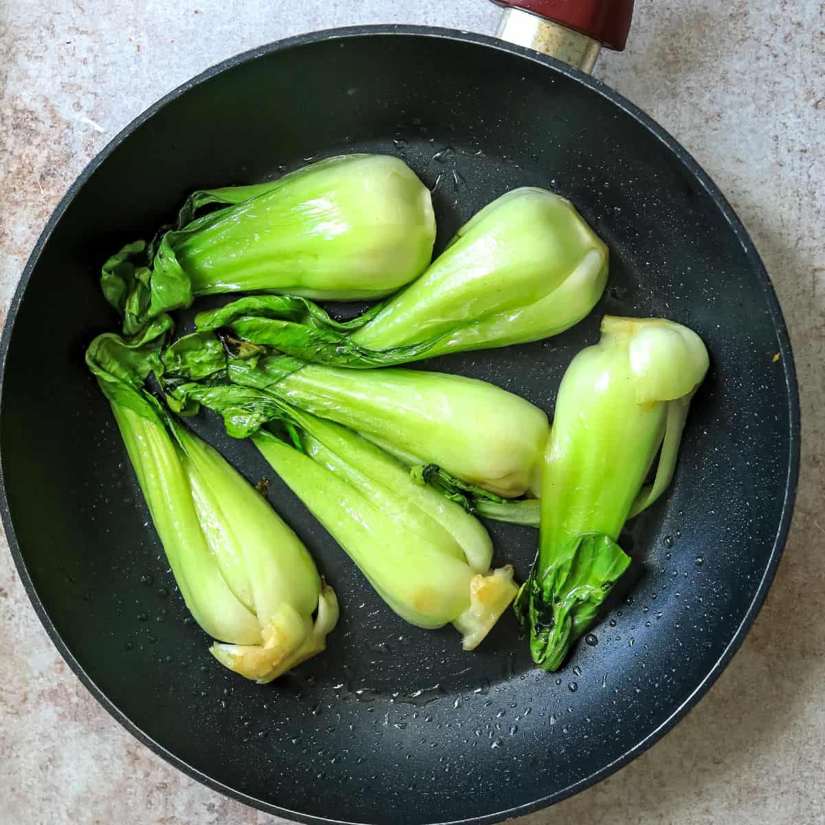 Black fry pan with sautéed baby bok choy in it.