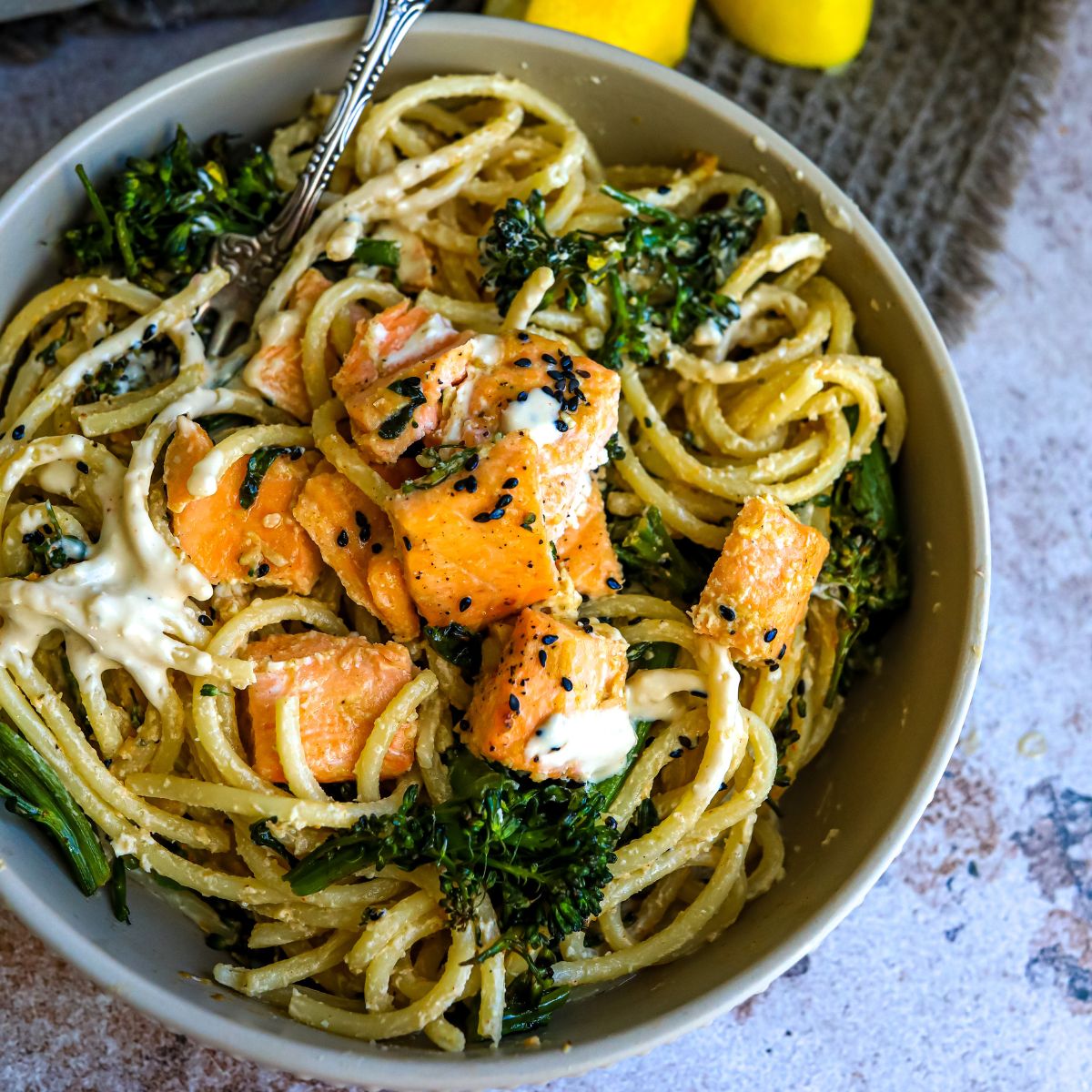 Saucy noodles with broccoli  and salmon in a grey bowl. 