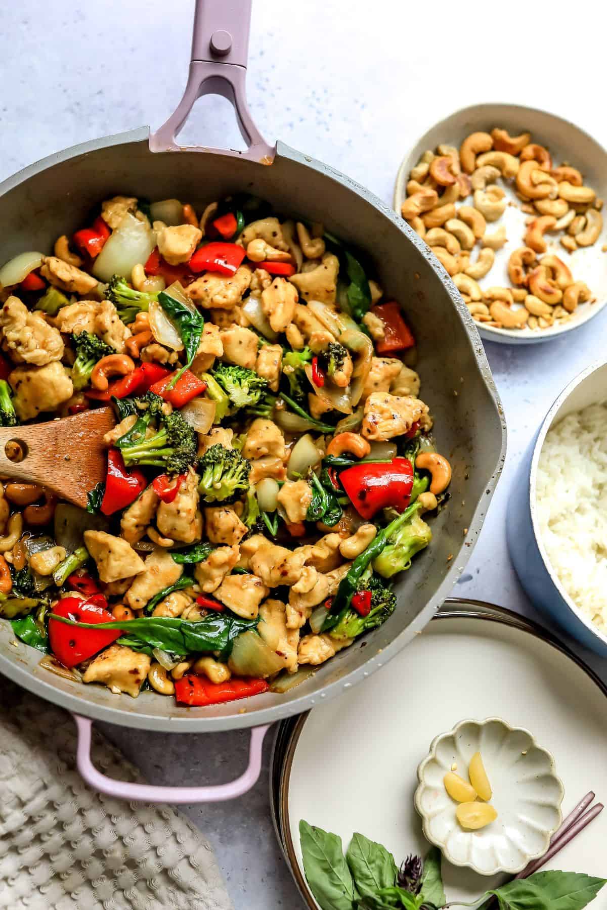 Chicken and veggies in a grey skillet up close with cashews to the side.
