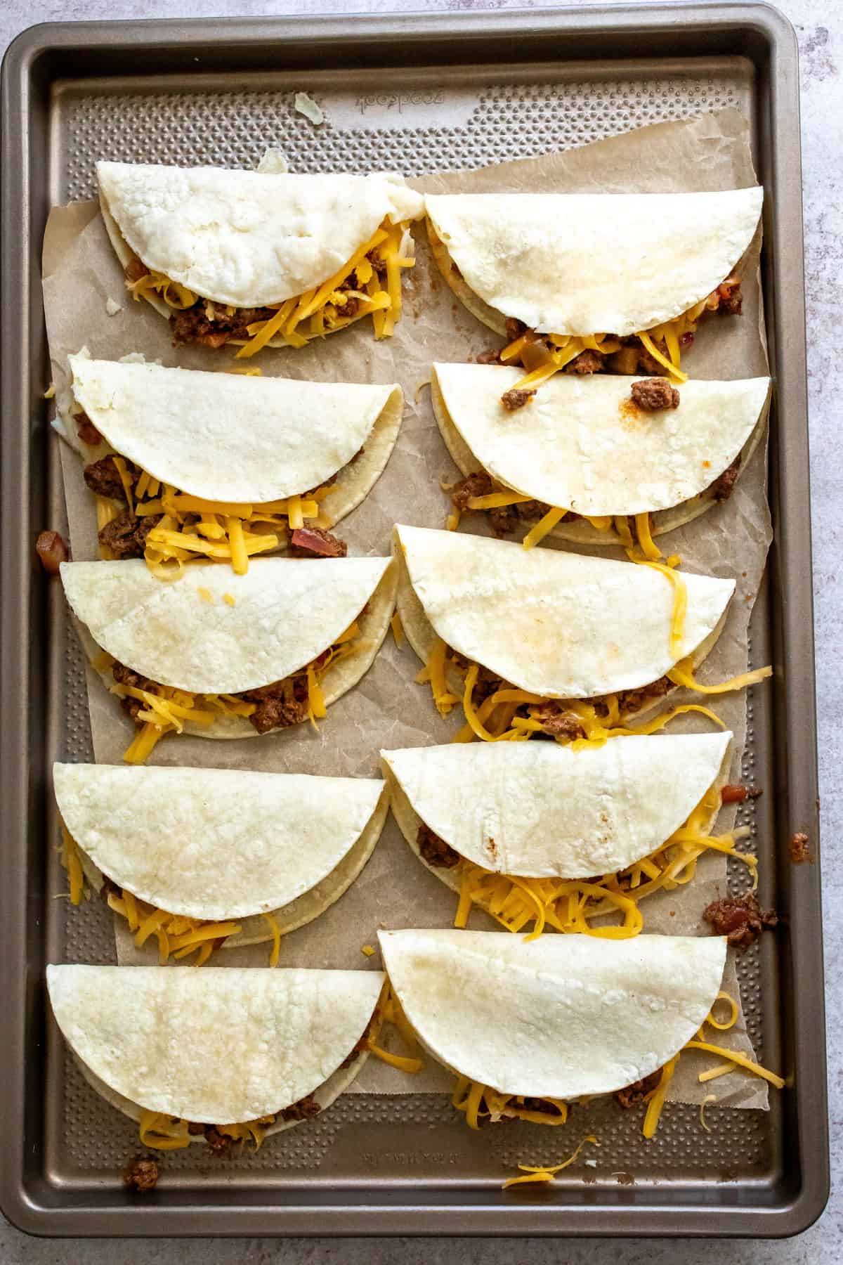 Steps to make the tacos on a cooking sheet with tortillas stuffed and folded. 