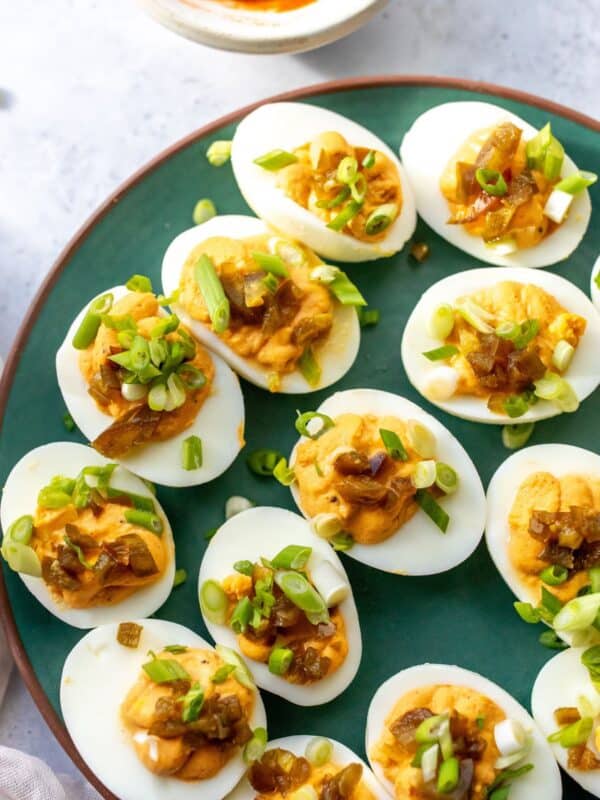 Deviled eggs on a green plate with toppings.