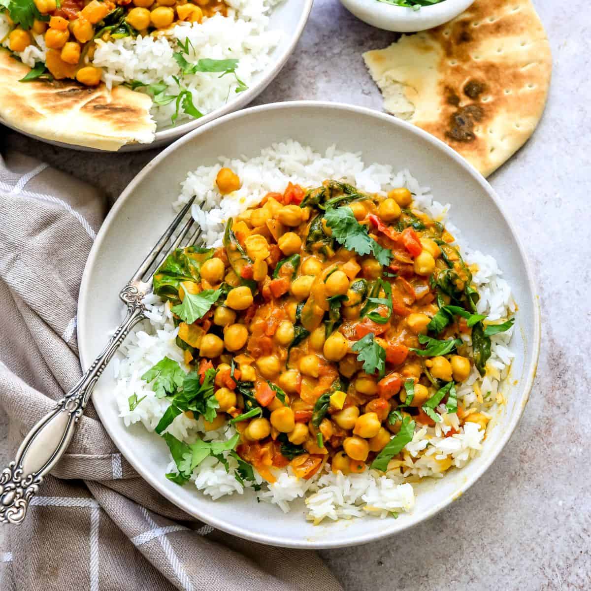 White ceramic bowls with Chickpea Spinach Curry in it and white rice.