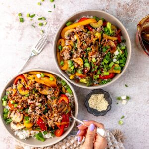 Two white bowls with ground beef stir fry in it and sauce to the side.