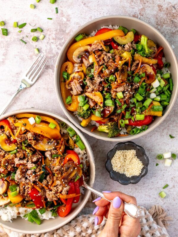 Two white bowls with ground beef stir fry in it and sauce to the side.