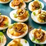 Deviled eggs on a green plate with toppings.