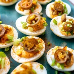 Deviled eggs on a green plate with toppings.