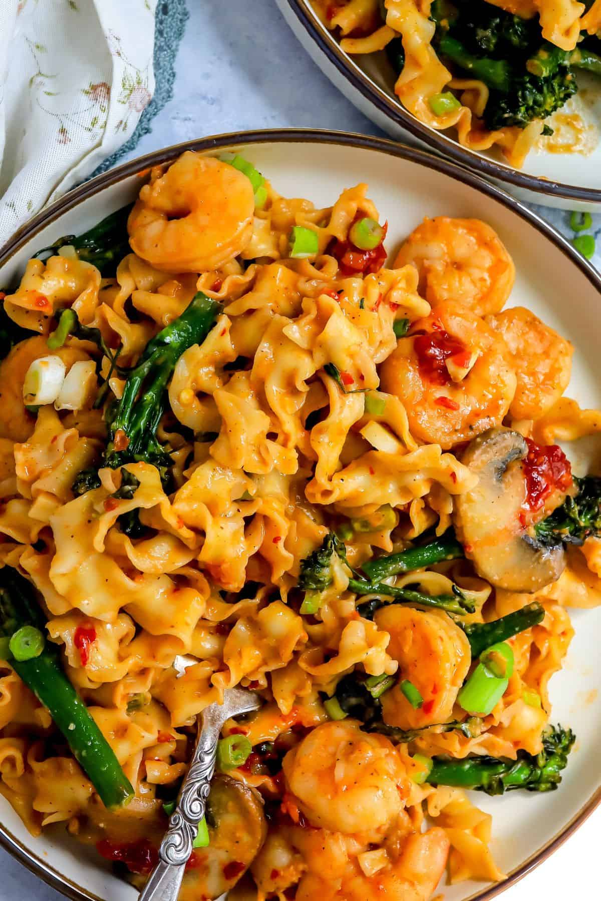 Miso shrimp over noodles with broccoli on a white plate with a fork.