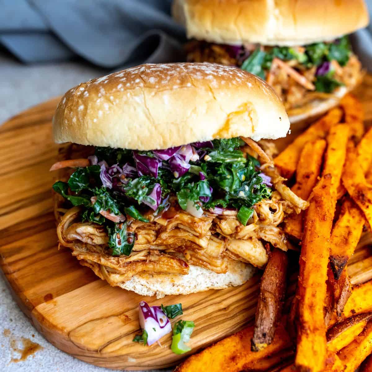 Pulled chicken sandwich on a cutting board  with a side of sweet potato fries.