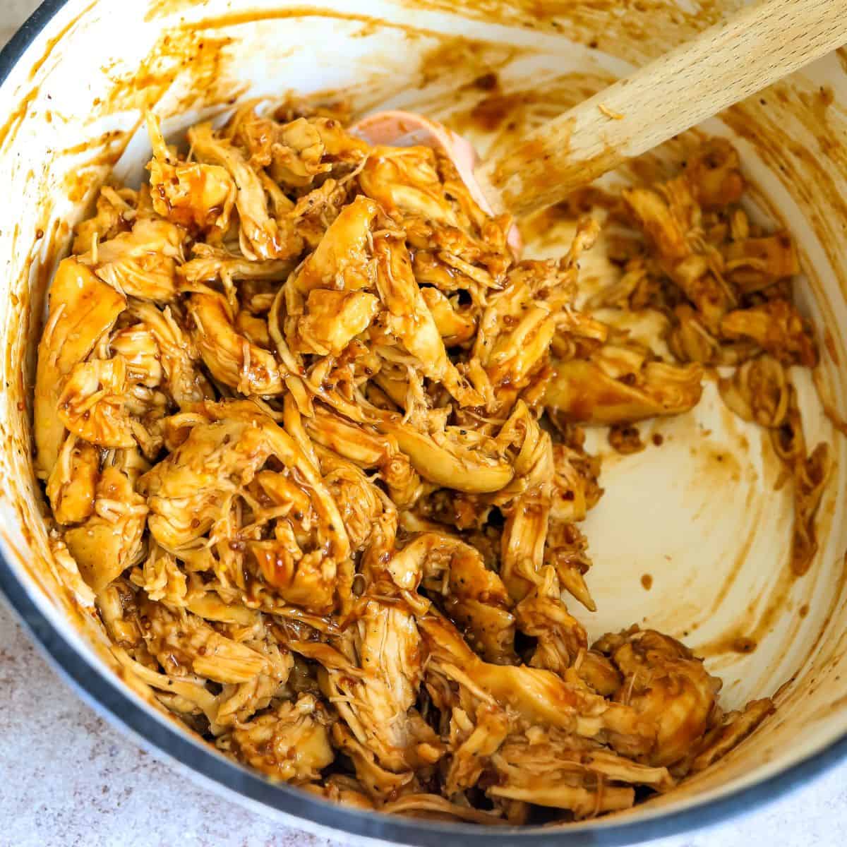 BBQ shredded chicken in a dutch oven with a spatula. 