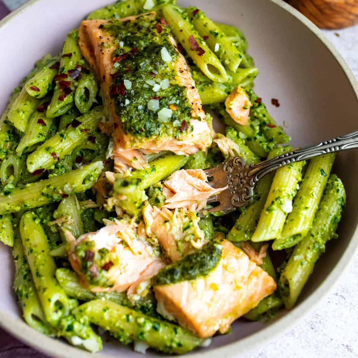 Salmon with pesto over pasta with a silver fork. 