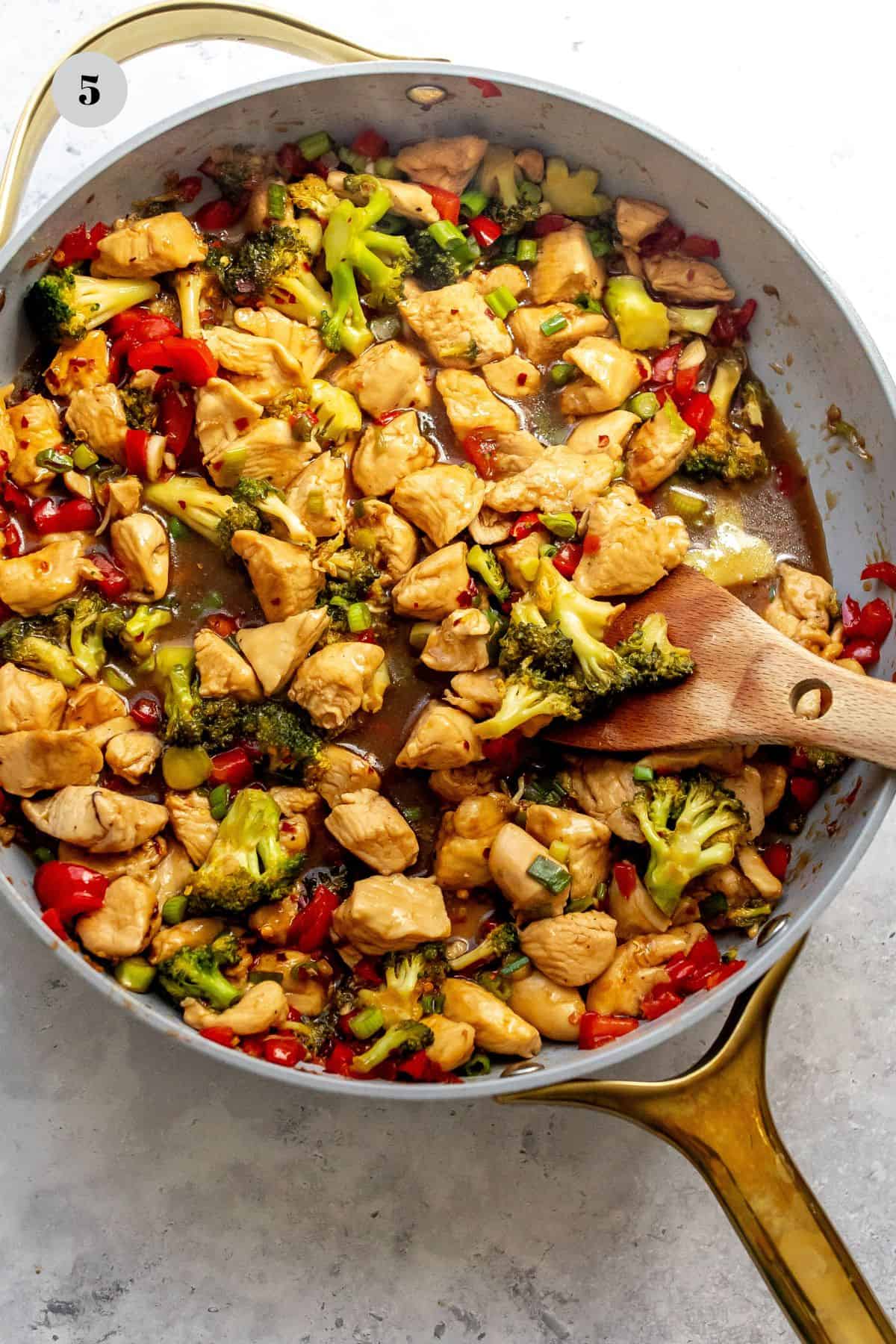 Grey skillet with teriyaki chicken in it and a wooden spoon.