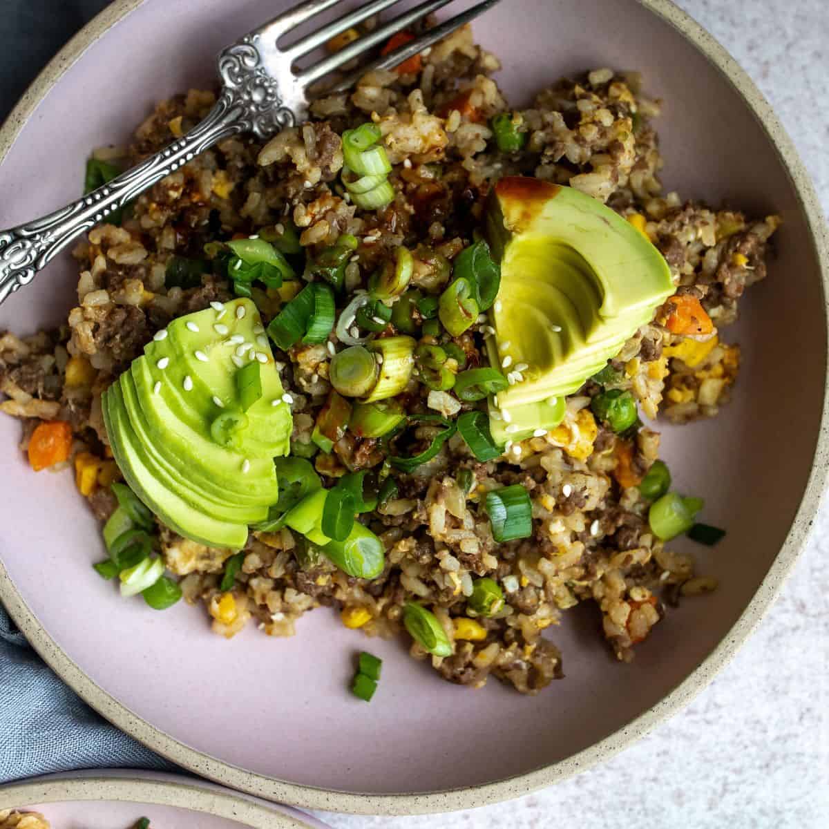  Hamburger fried rice in a pink bowl topped with green onions and sliced avocado.