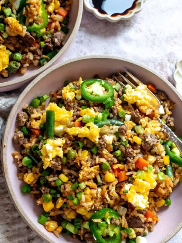 Pink bowl with ground beef fried rice in it, soy sauce to the side.