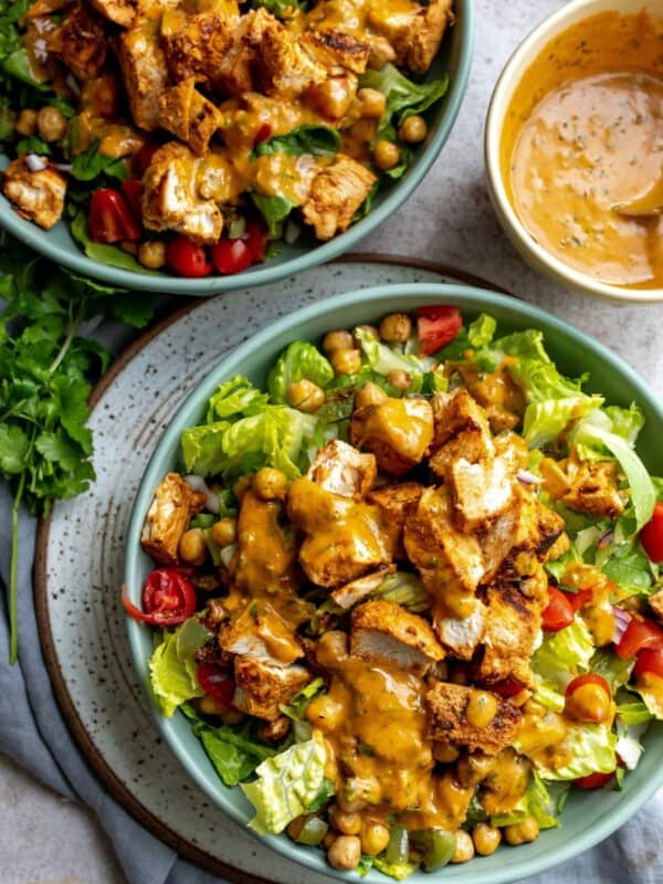 Two bowls with salad, tomatoes and chicken in it.