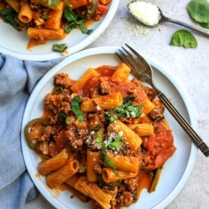 White plate with saucy noodles and pepperonis.