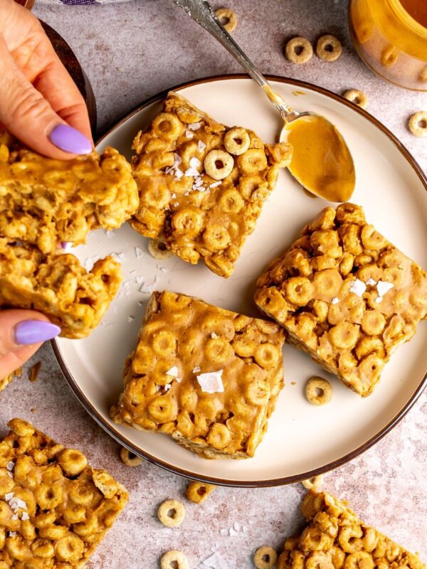 peanut butter and cheerio bars on a white plate with peanut butter on a spoon.