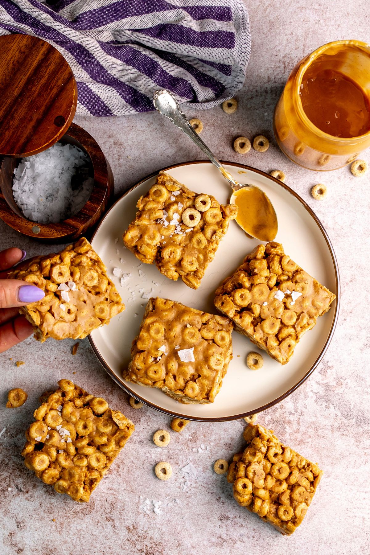 peanut butter and cheerio bars on a white plate with peanut butter on a spoon.