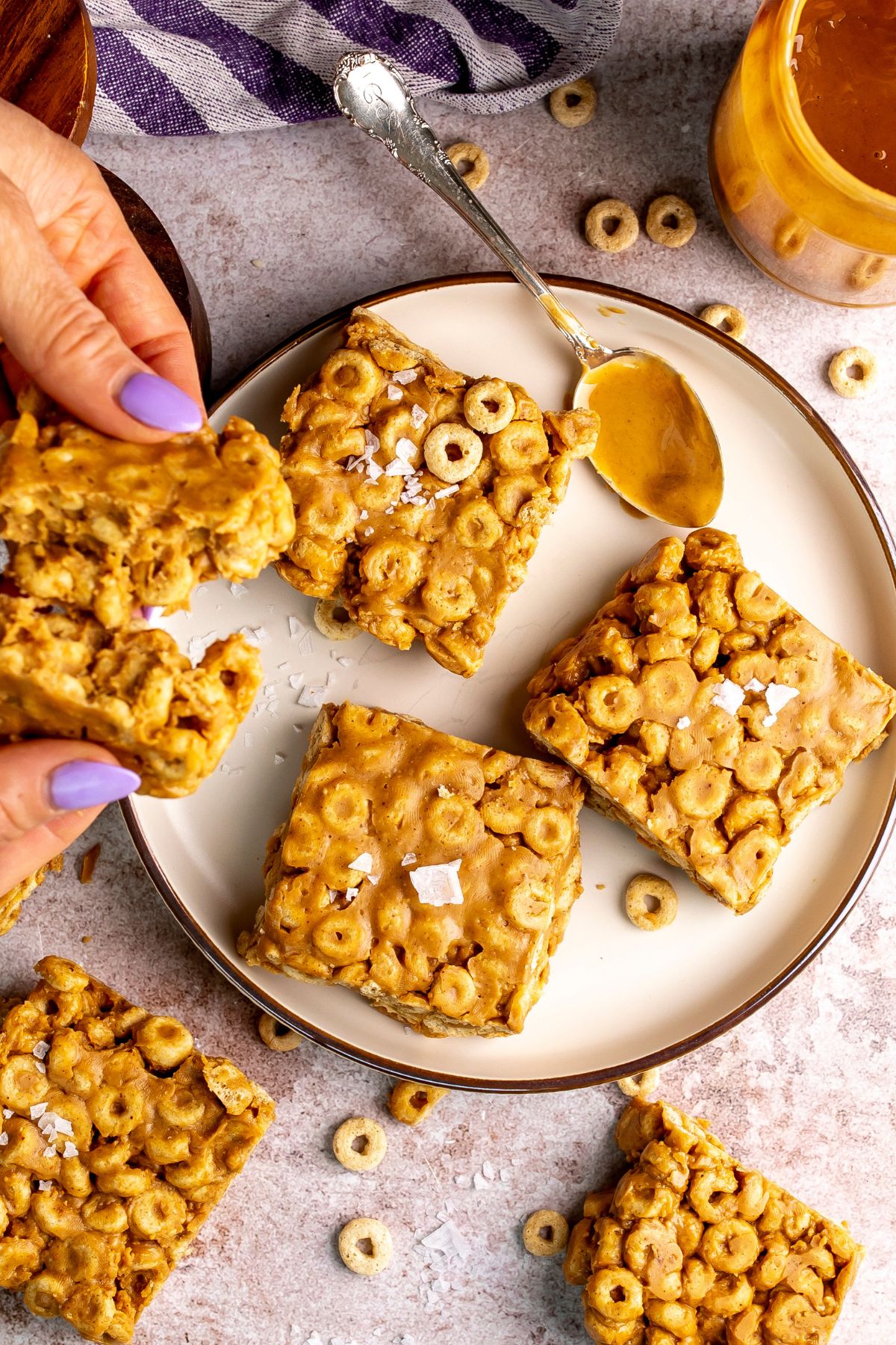 peanut butter and cheerio bars on a white plate with peanut butter on a spoon.