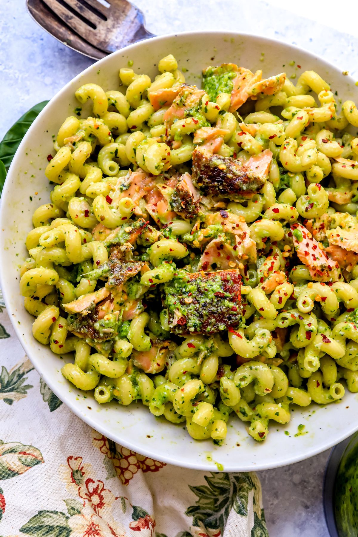 pesto pasta and salmon in a white dish and a towel to the side.