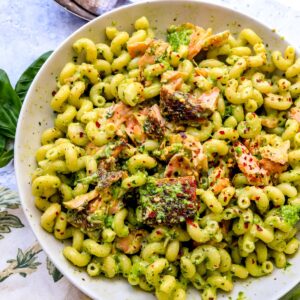 pesto pasta and salmon in a white dish and a towel to the side.