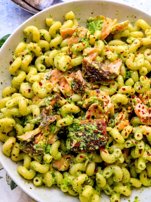 pesto pasta and salmon in a white dish and a towel to the side.