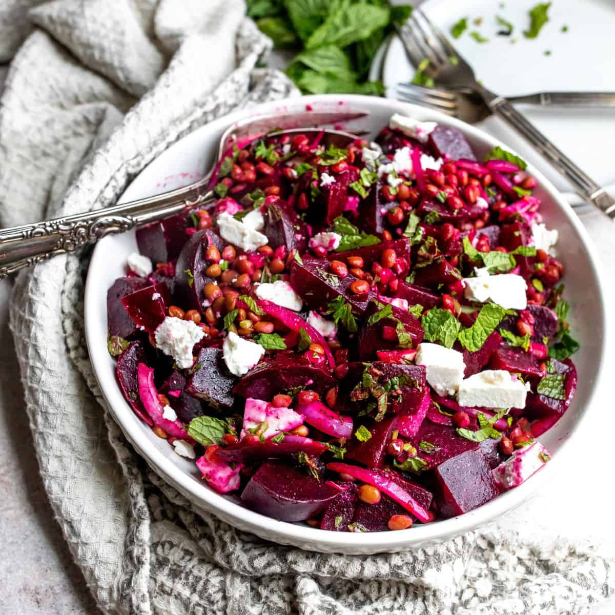 White bowl with beets and feta, a silver fork and a towel. 