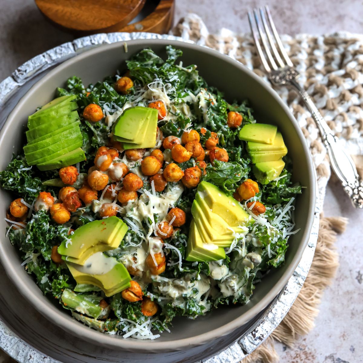 Kale and chickpea salad with toppings in a grey bowl with a fork. 