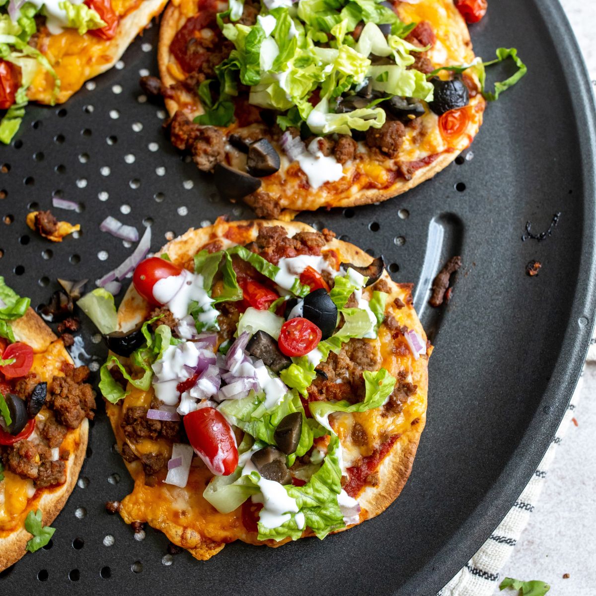 Tortilla pizzas on a pan with lots of toppings and melted cheese.