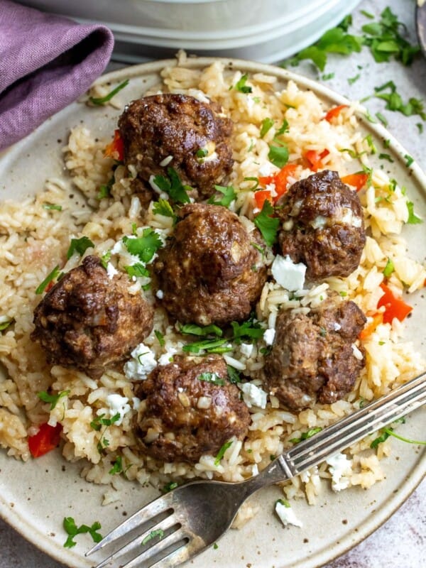 White plate with a silver fork and rice and meatballs.