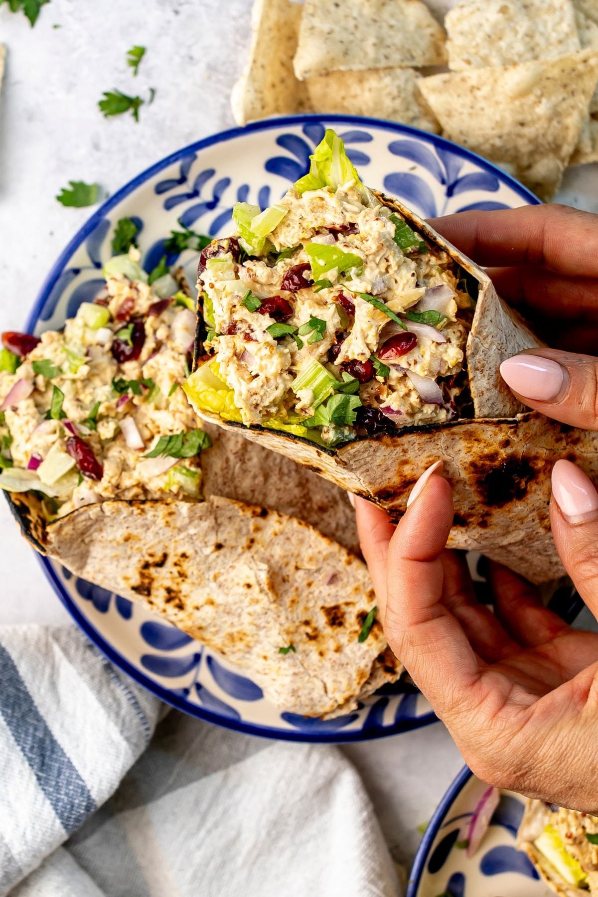 A hand holds a chicken salad wrap over a blue and white plate with another chicken salad wrap on it.