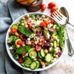 Greek cucumber salad in a white bowl on a table with silver serving utensils to the side.