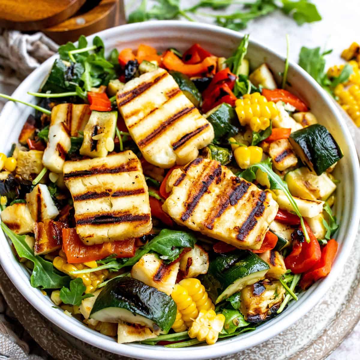 Zucchini salad with grilled halloumi in a white bowl on a counter. 