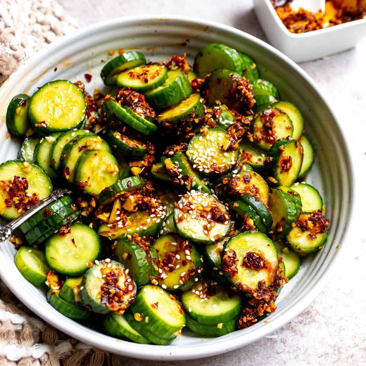 White bowl full of green cucumbers and red chili onion crunch. 