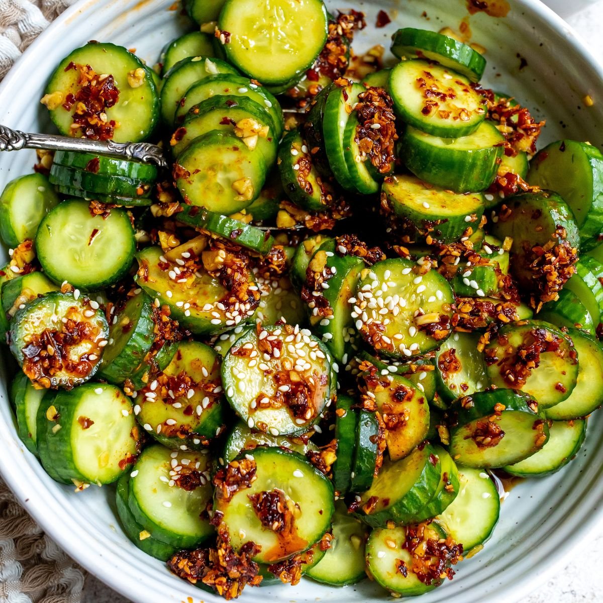 White bowl with green cucumbers and sesame seeds. 