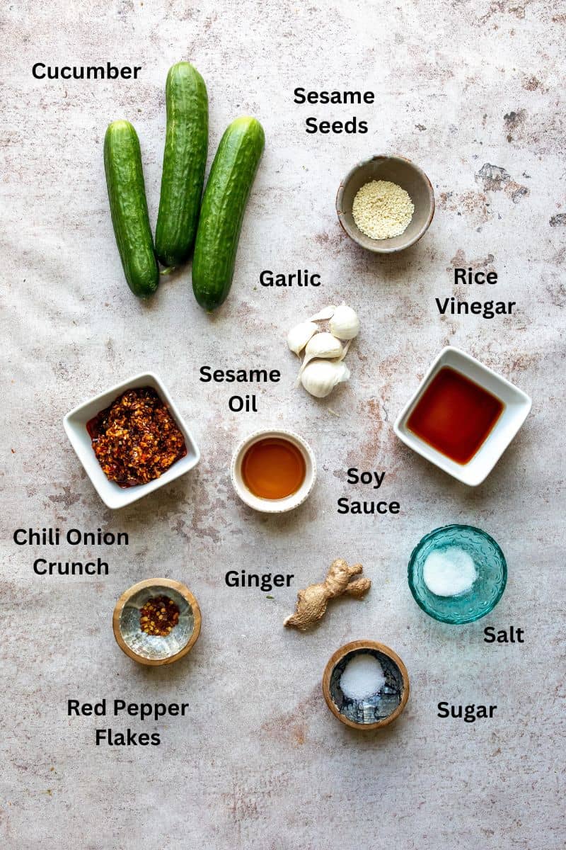 All Ingredients needed to make spicy korean cucumber salad on a counter in small bowls and plates.
