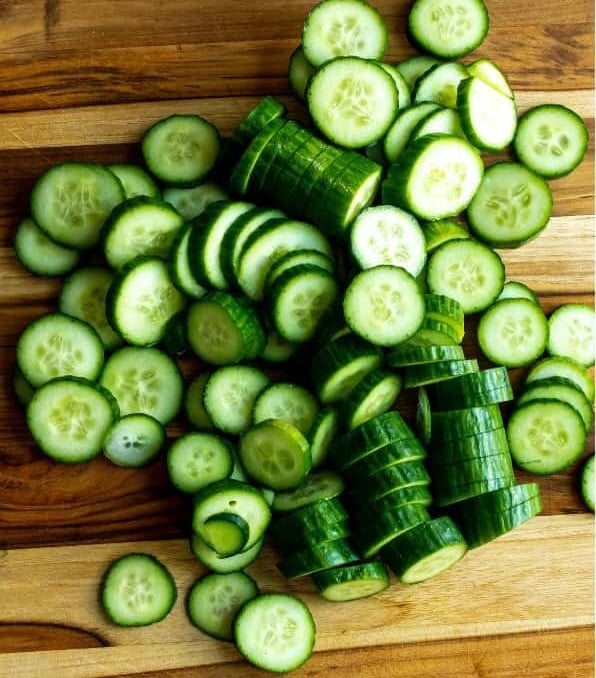 Sliced persian cucumbers on a wooden cutting board.